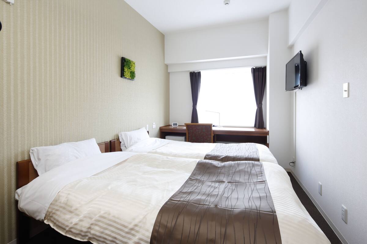 Quarto de hotel com uma cama grande, escrivaninha, televisão e janela com cortinas.