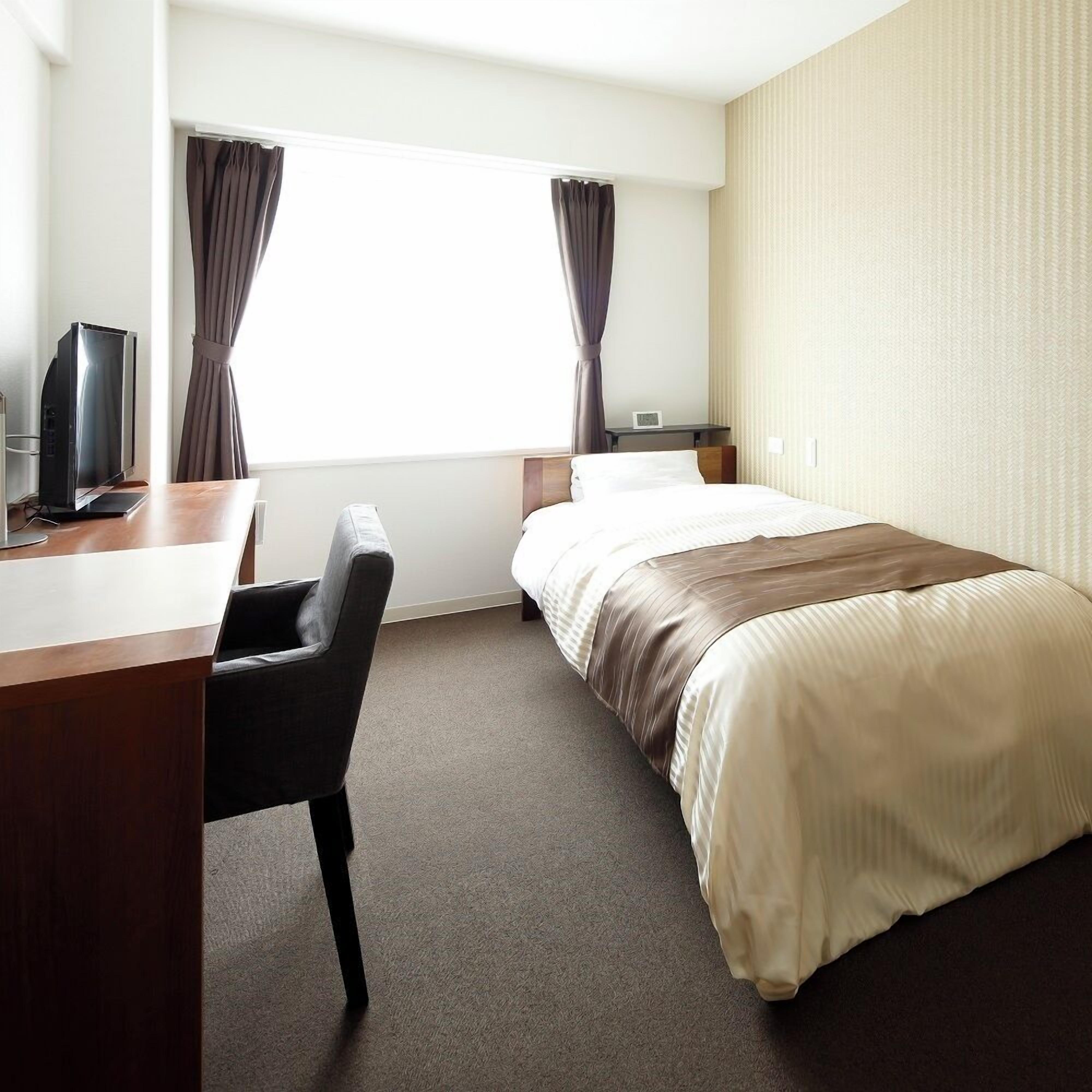 A hotel room with a bed, a desk, a chair, a television, and curtains.