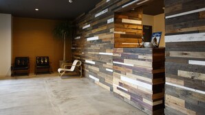 A reception area with a wooden wall, a concrete floor, and a few chairs. - Kyou Bar Lounge & Inn (Sendai)