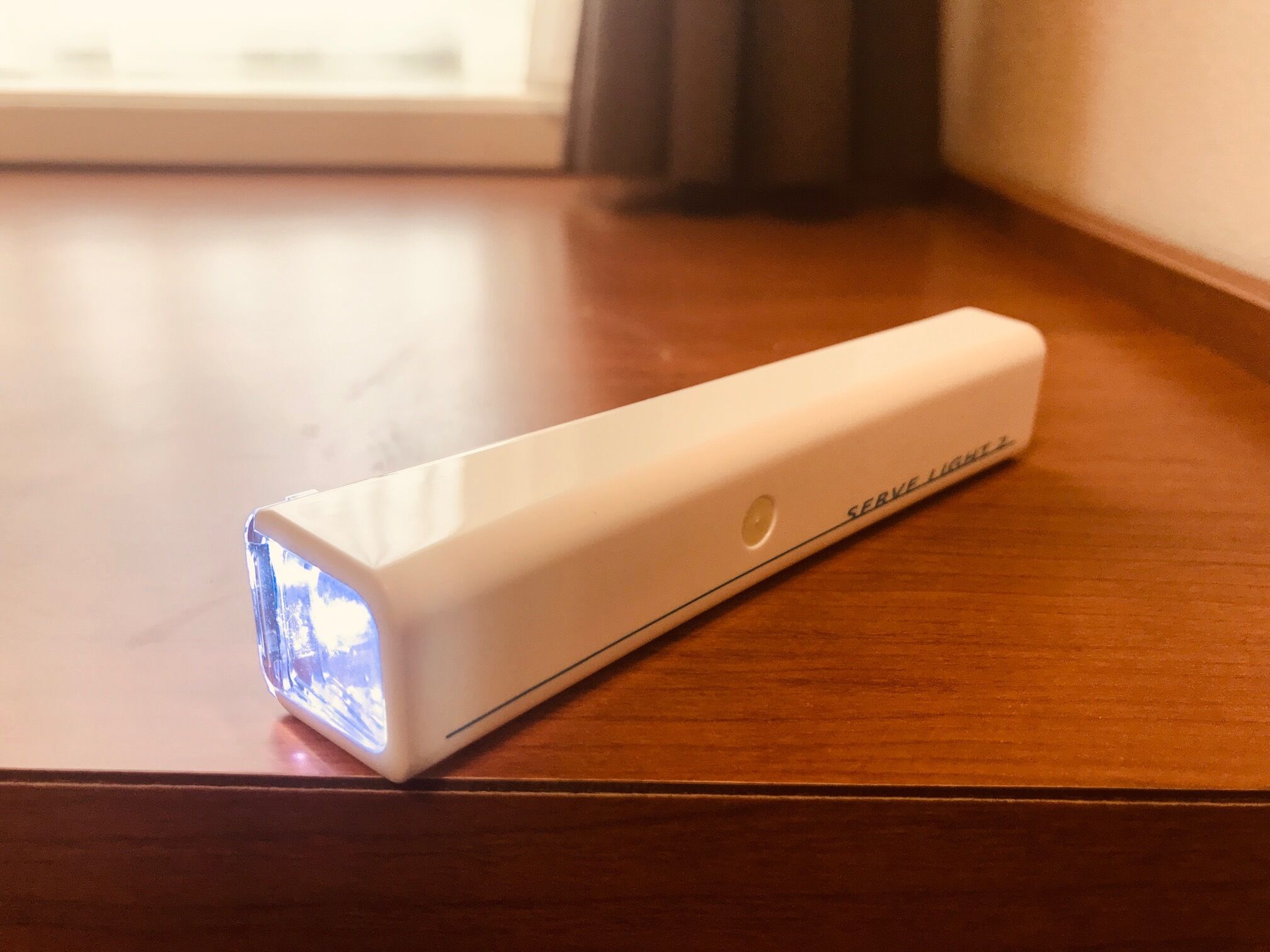 A white portable device with a blue light on a wooden surface.