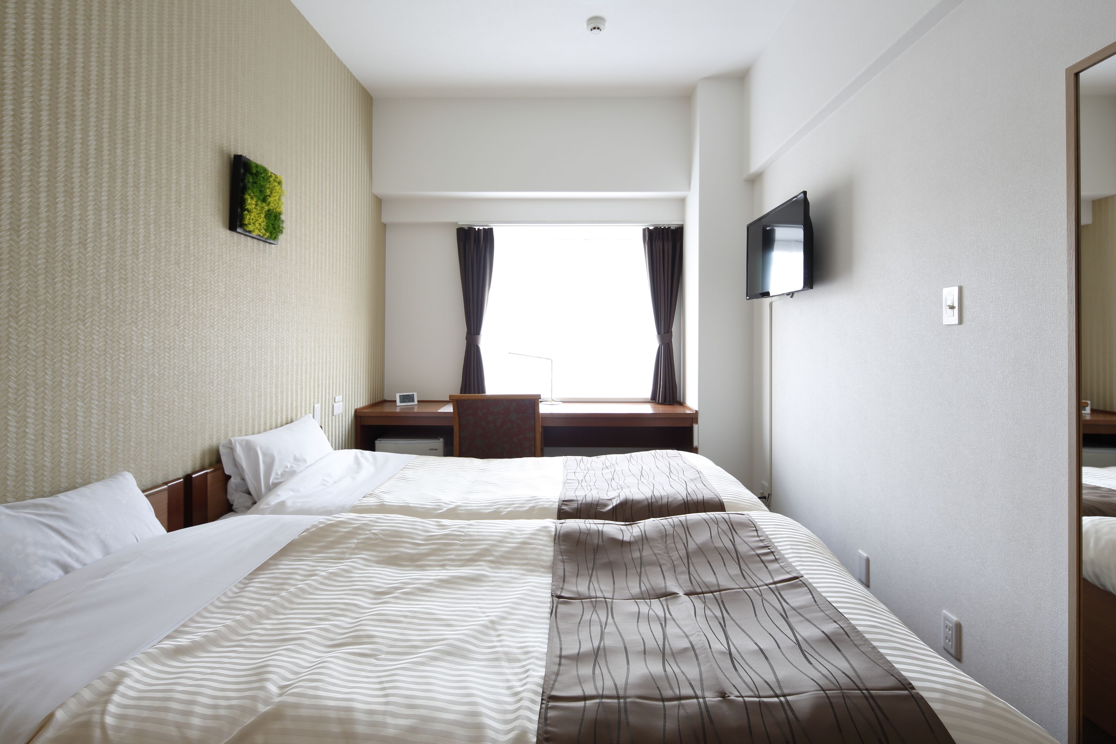 A hotel room with a large bed, a desk, a chair, a TV, and a window with curtains.