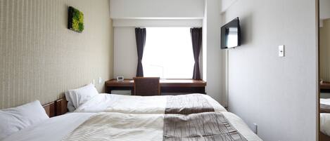 A hotel room with a large bed, a desk, a chair, a TV, and a window with curtains.