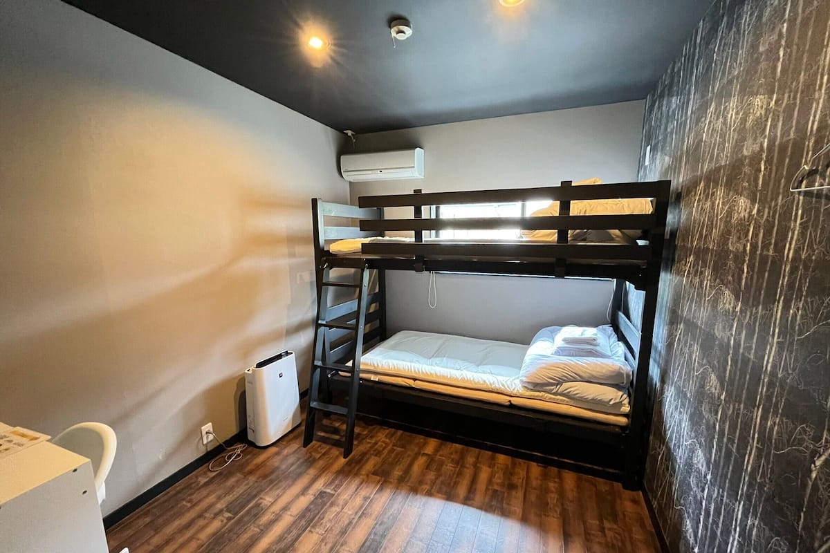 Quarto com beliches, piso de madeira, ar condicionado branco e parede com padrão marmorizado.