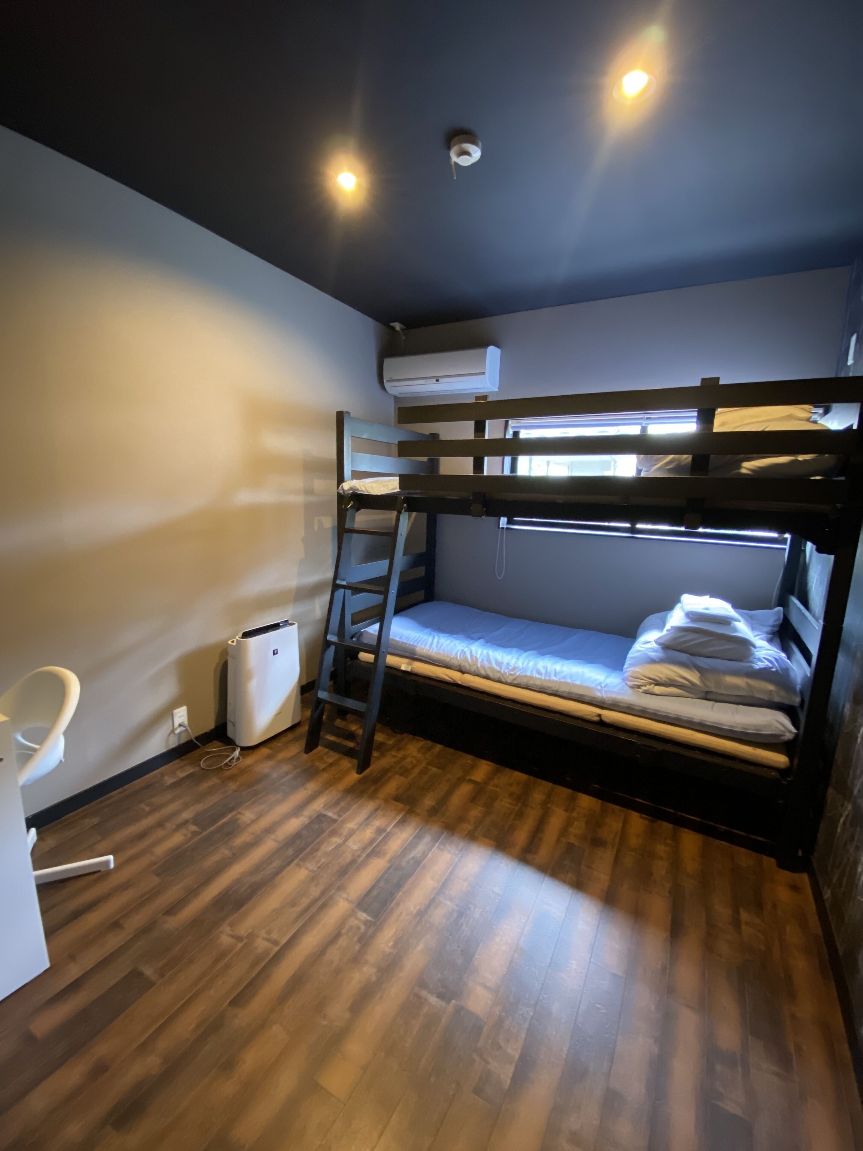 A bunk bed room with a wooden floor, a white chair, and an air conditioning unit.