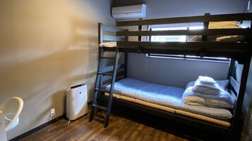 A bunk bed room with a wooden floor, a white chair, and an air conditioning unit.