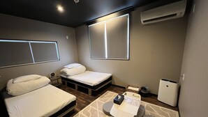 A compact hotel room with a bed, bedside table, air conditioning unit, and a small seating area with a table and chairs. - Hostel&Information SAMURISE (Fujikawaguchiko)