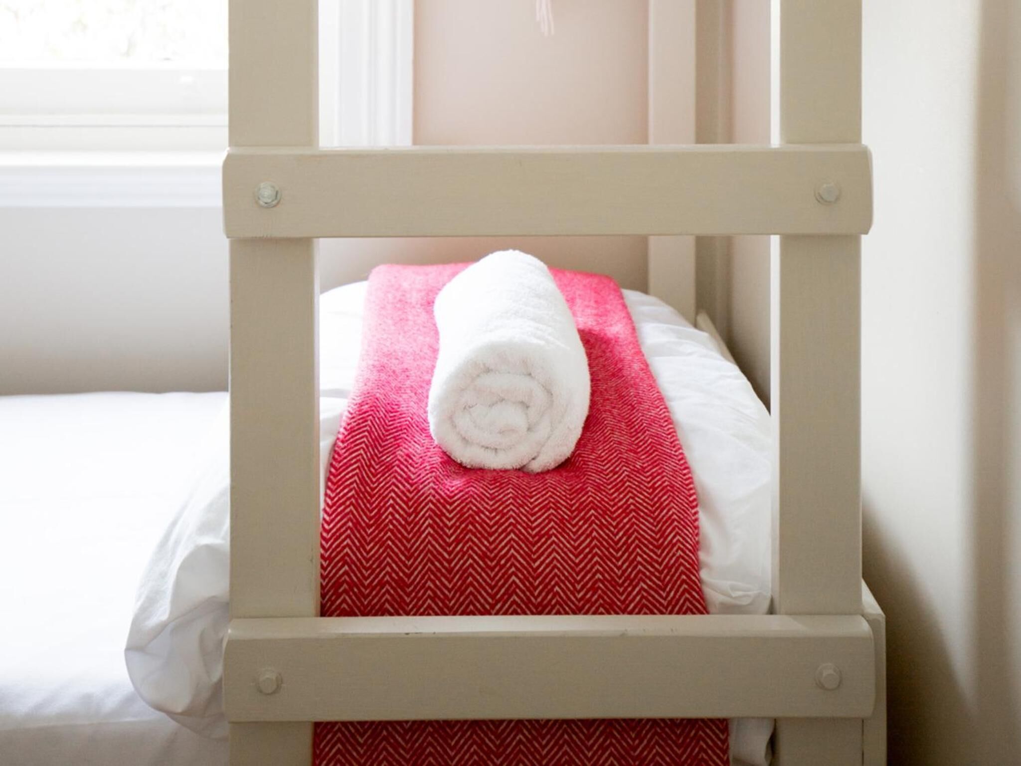 Un lit bien fait, avec une serviette blanche roulée et une couverture à motifs rouges et blancs.