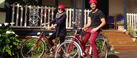 Dos personas en bicicleta frente a un edificio con porche y barandilla decorativa.