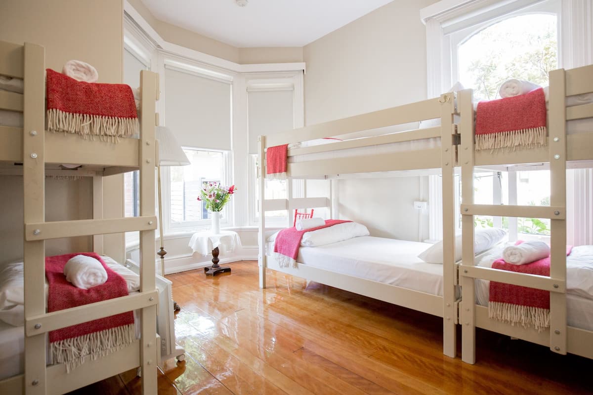 A room with bunk beds, a small table with a vase of flowers, and a window providing natural light.