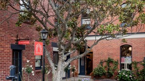 Un edificio de ladrillo con un cartel de recepción, un árbol en primer plano y un jardín bien cuidado con diversas plantas y flores.