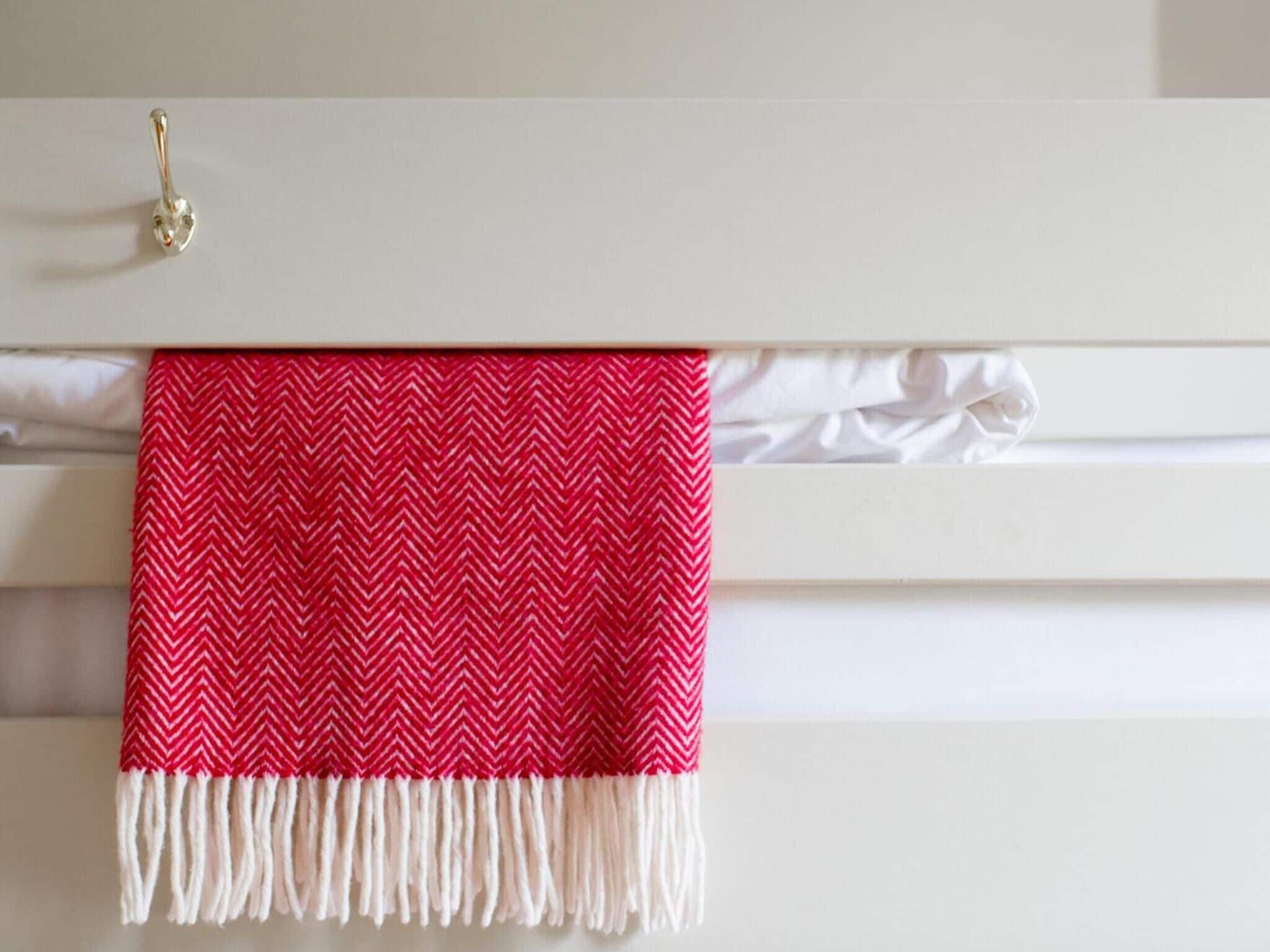 A white wall with a red and white patterned towel hanging on a white towel rack.