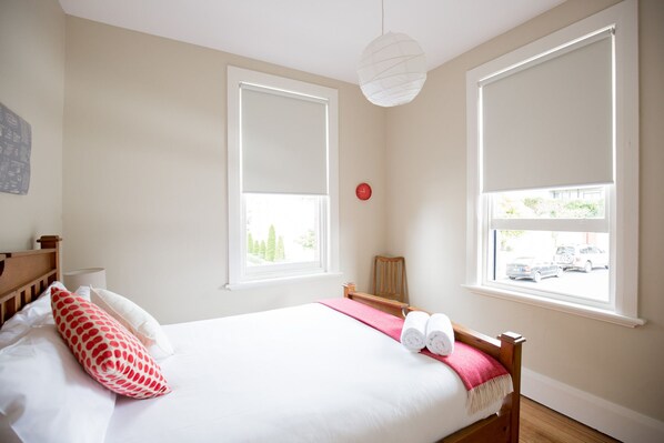 A bedroom with a bed, a wooden headboard, a red clock, and two windows with blinds.