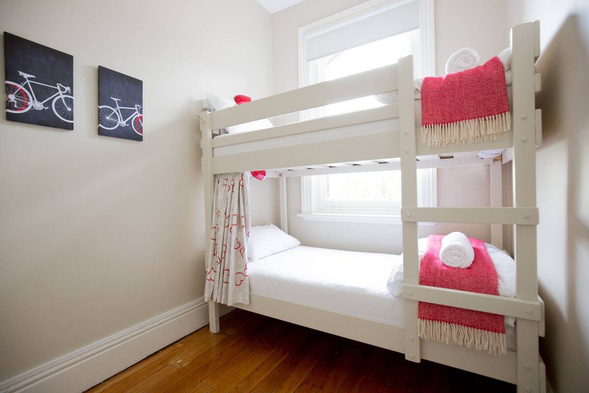 A bunk bed with a window, white walls, and two framed pictures on the wall.
