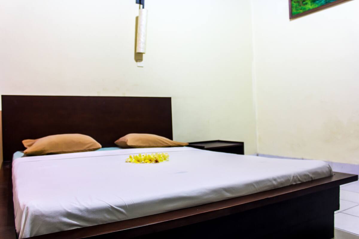 A bed with a white sheet, two pillows, and a small yellow flower arrangement.
