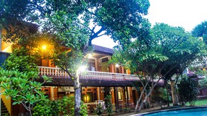 A traditional building with a balcony, surrounded by lush greenery and a swimming pool. - Budhi Beach Inn (Kuta)