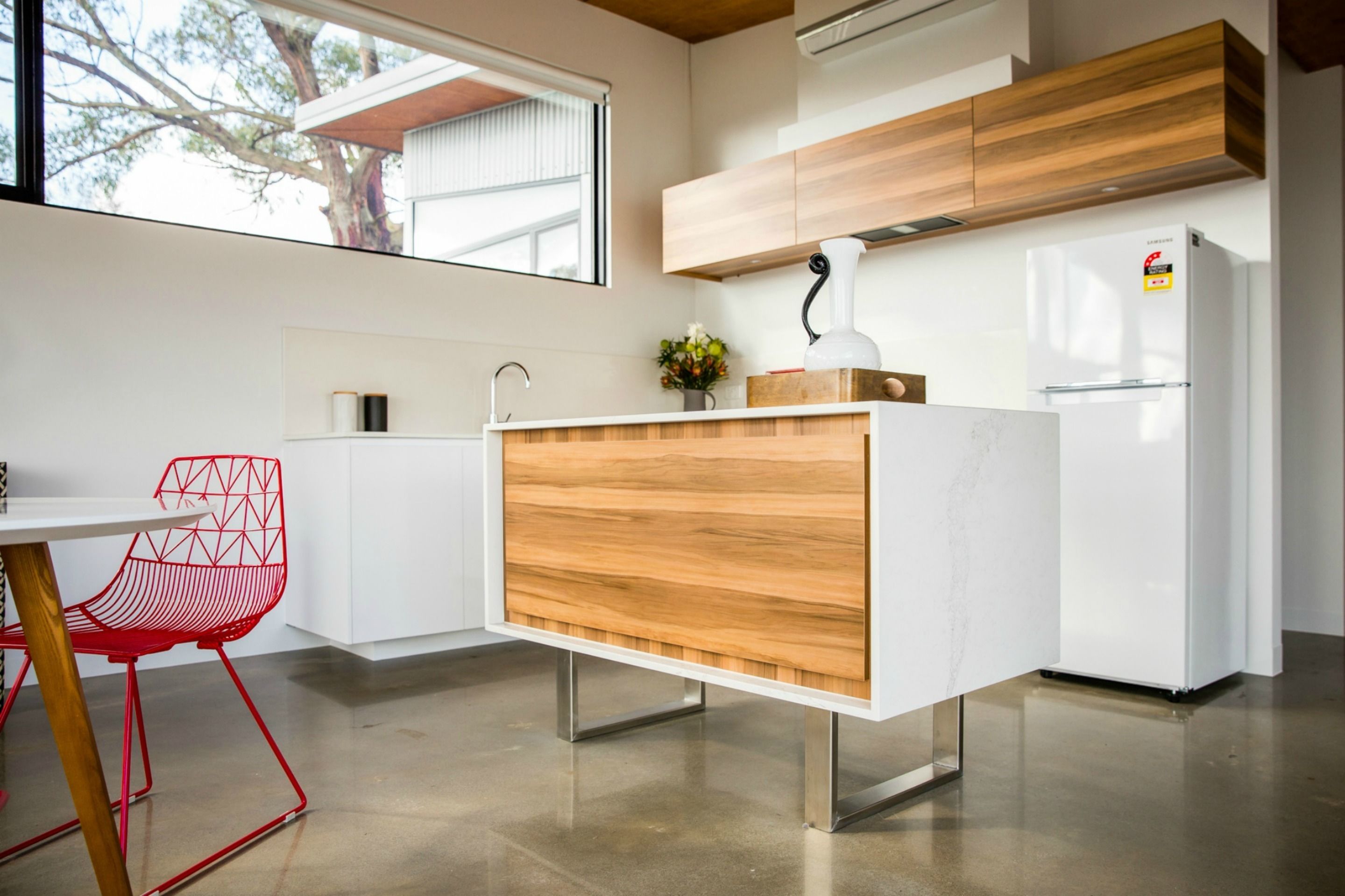 A modern kitchen with white cabinetry, a wooden countertop, a red chair, and a white refrigerator.