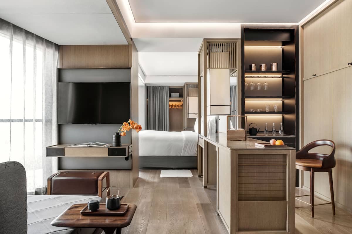 Une chambre d’hôtel moderne équipée d’un lit, d’une télévision, d’un bureau avec une chaise, d’un petit coin cuisine et d’un espace salon avec une table et des chaises.