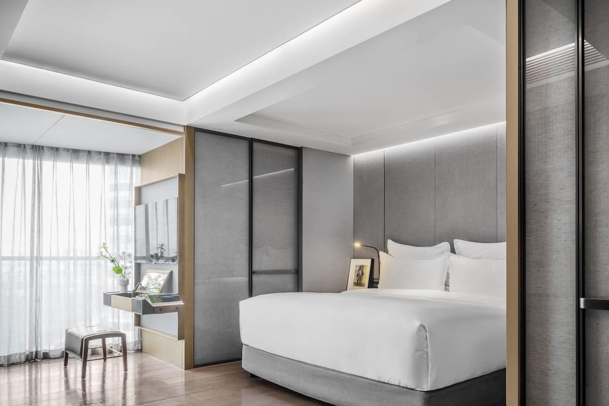 Une chambre d’hôtel moderne dotée d’un grand lit, d’un bureau avec une chaise et offrant une vue sur l’extérieur grâce à une grande fenêtre.