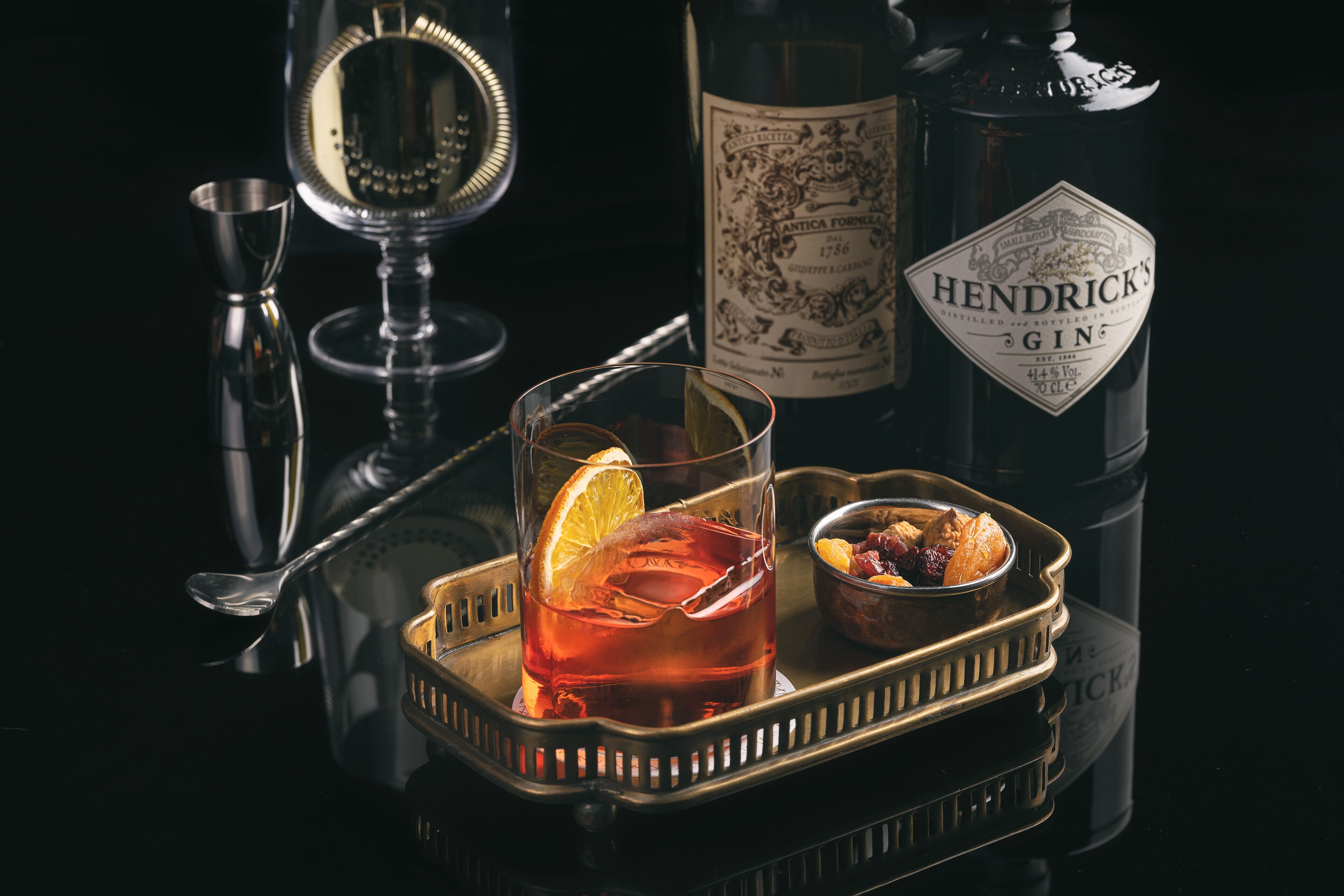 Un plateau avec un verre de gin Hendrick's, un petit bol de collations et un shaker à cocktails.