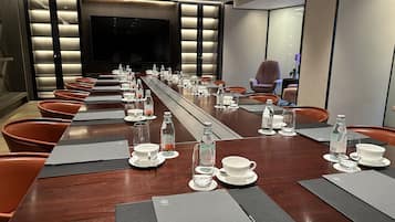 A conference room with a long table set for a meeting, equipped with water bottles, cups, and place mats.