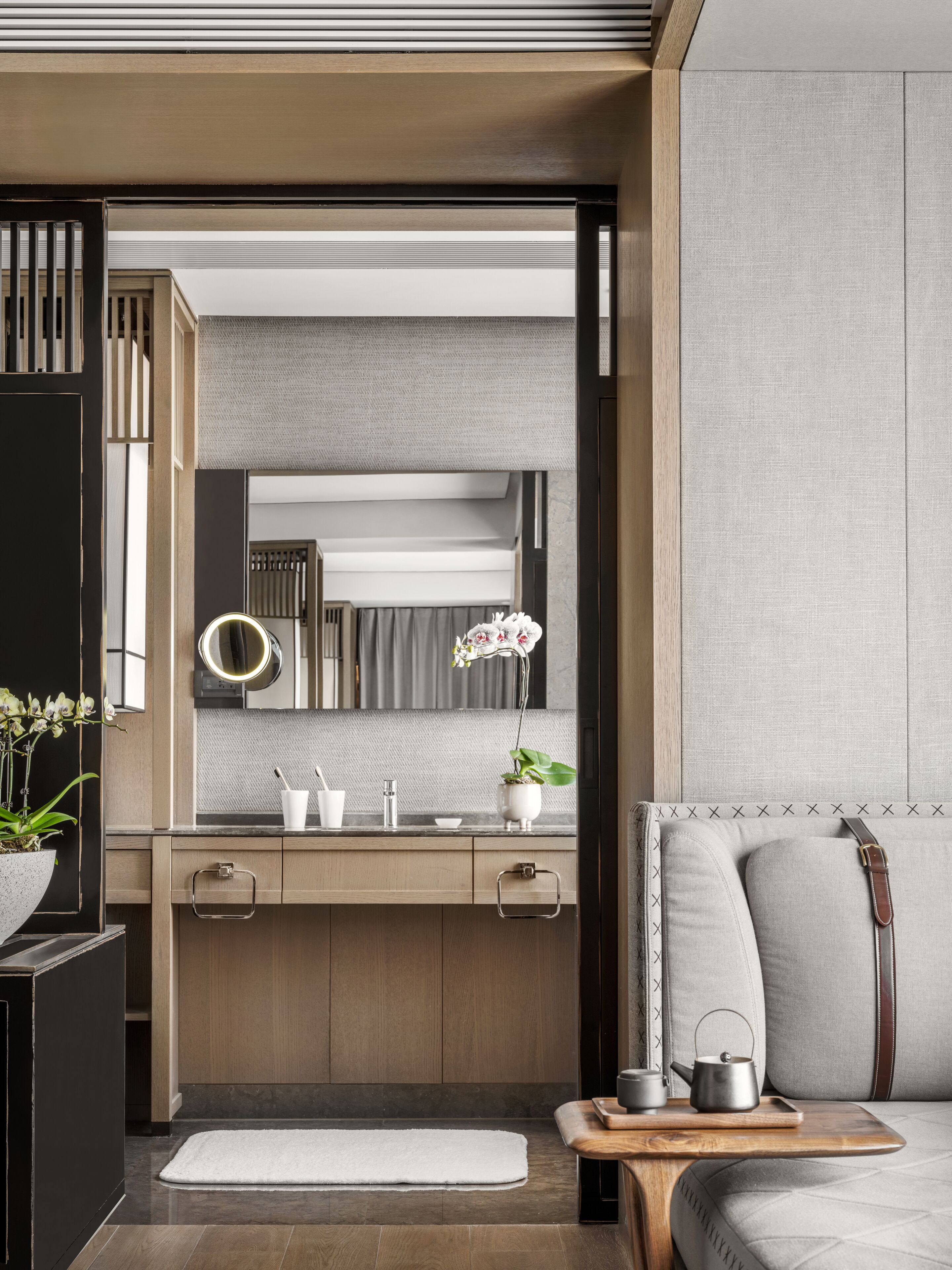 A modern bathroom with a wooden vanity, a mirror with lights, a sink, and a small plant.
