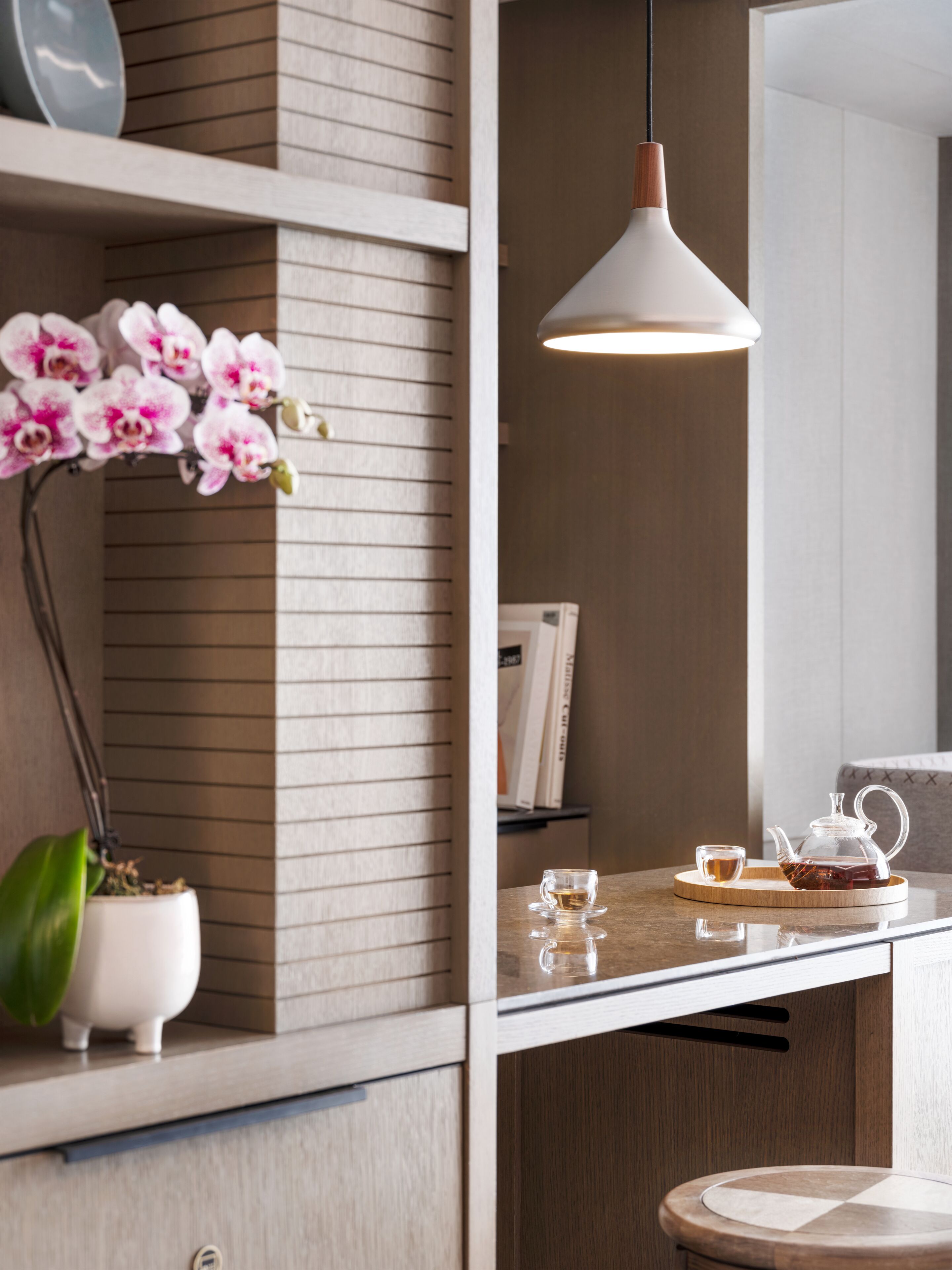 Une cuisine moderne avec un plan de travail en bois, une suspension décorative, une orchidée en pot et un service à thé posé sur la table.