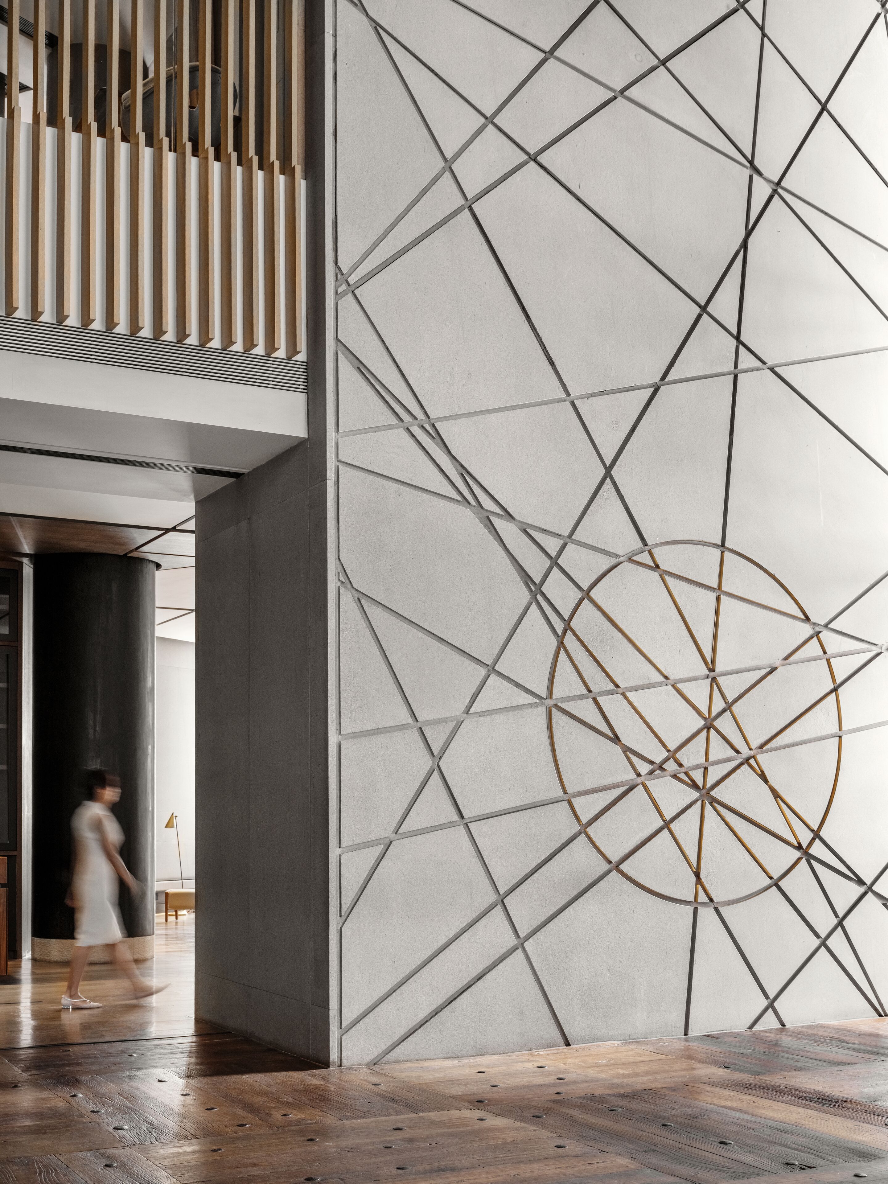 Un intérieur moderne avec un motif géométrique sur le mur, un plancher en bois et une personne qui marche.