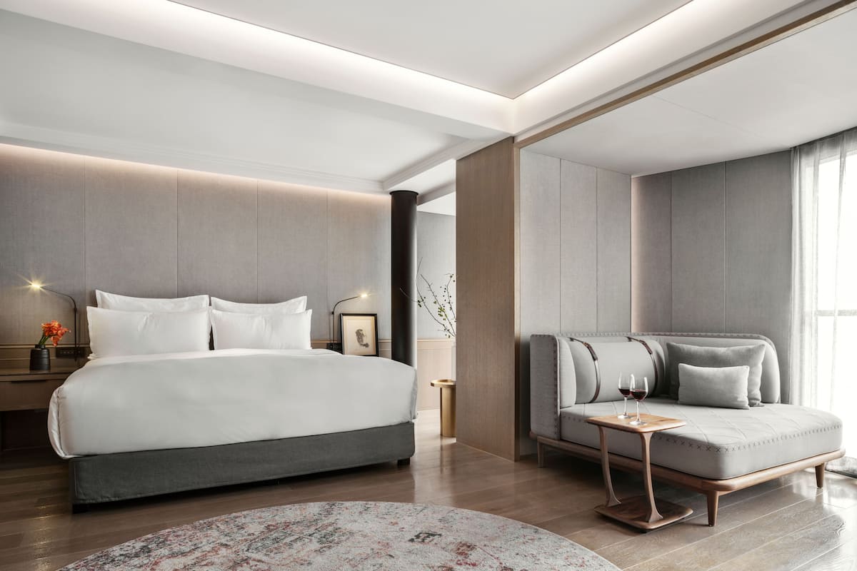 Une chambre d’hôtel moderne, dotée d’un grand lit, d’un canapé, d’une petite table et d’une table de chevet avec une lampe et un vase.