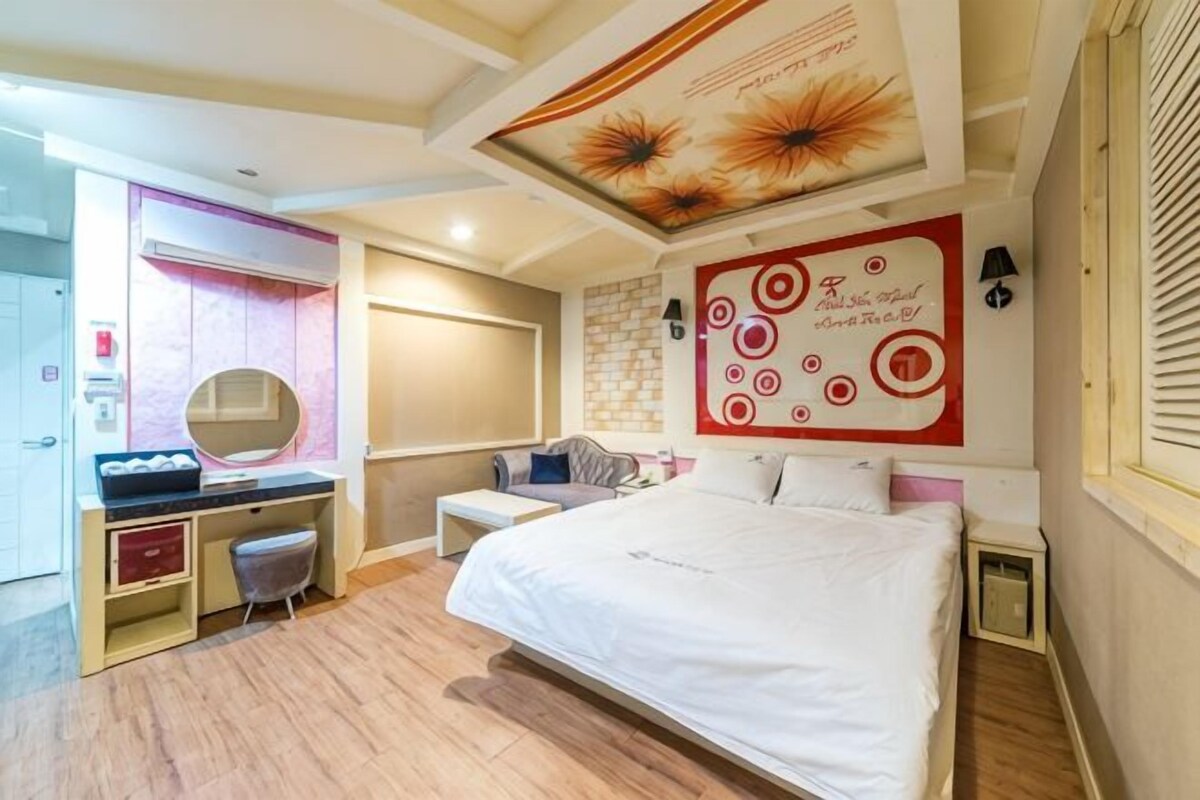 Quarto com cama, escrivaninha, cadeira, espelho e parede com um desenho circular.