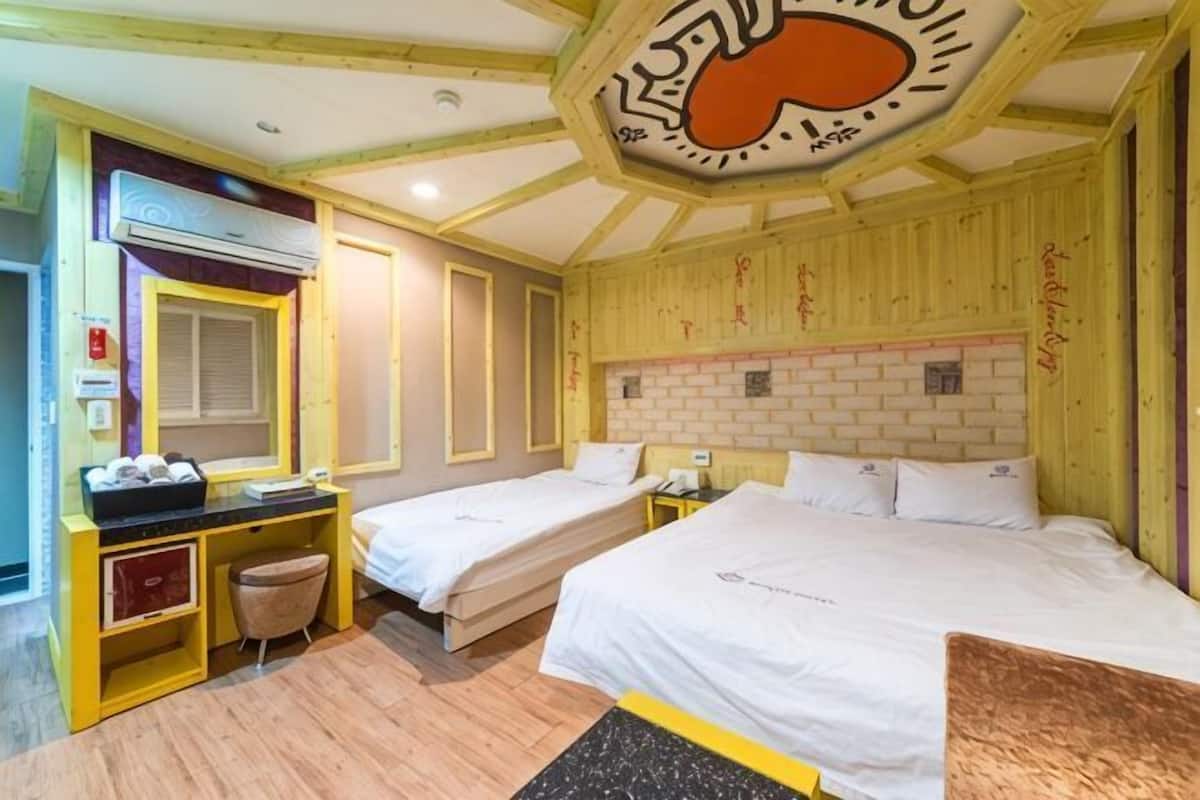 A hotel room with two beds, a desk with a chair, a small seating area, and a unique ceiling design.