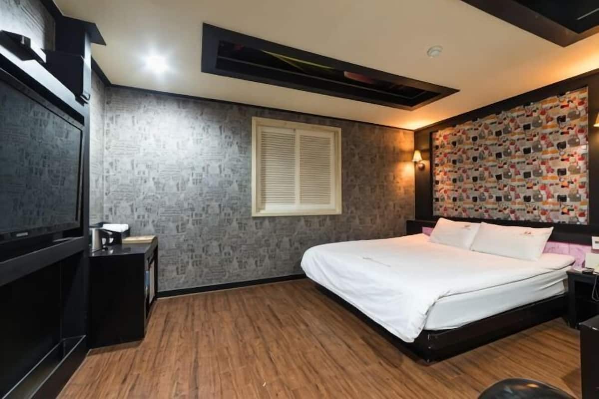A bedroom with a bed, a nightstand, a TV, and a wall with a patterned design.