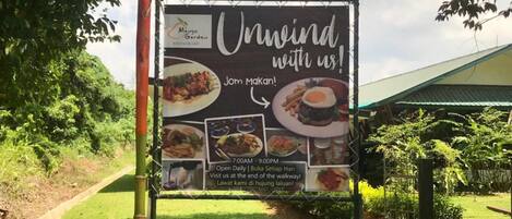 A restaurant signboard advertising 'Mango Garden Restaurant' with a menu of dishes and operating hours.