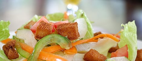 Un plato de ensalada con crotones y verduras, y un vaso de jugo de naranja al fondo.