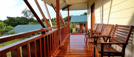 A wooden porch with benches, a red carpet, and a view of a house and greenery.