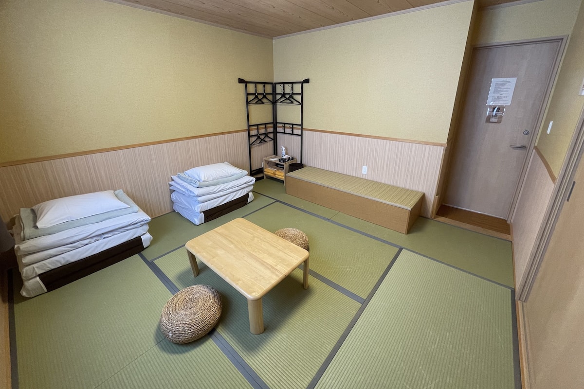 A room with a bed, a bench, a small table, and a hanging rack.