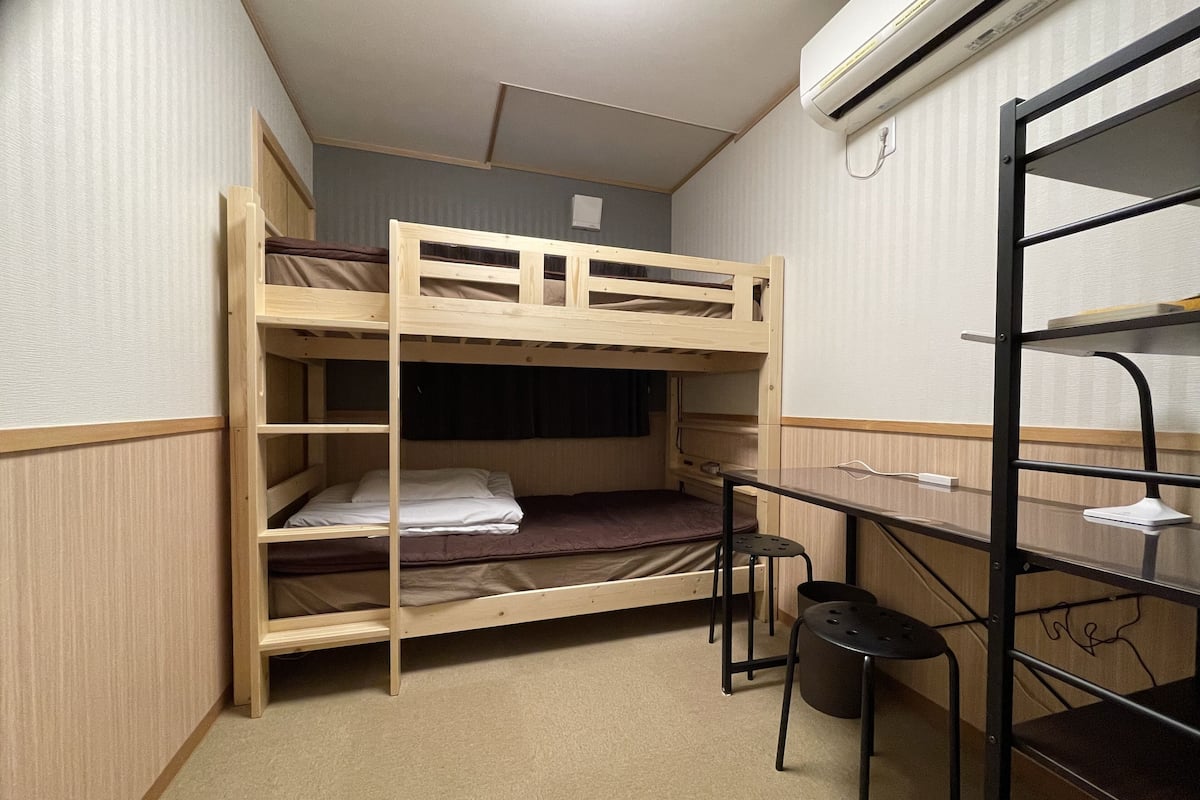 A bunk bed room with a desk and chair, a small stool, and a shelf unit.