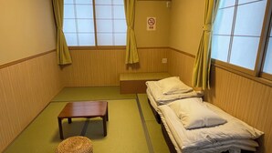 A small, traditional Japanese-style room with tatami flooring, two single beds, a small wooden table, and a woven mat. - Guesthouse OC (Fujikawaguchiko)