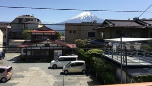 A residential area with traditional Japanese architecture, a parking lot with cars, and a view of Mount Fuji in the background. - Guesthouse OC (Fujikawaguchiko)