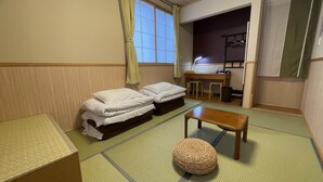 A traditional Japanese-style room with tatami mats, two single beds, a wooden table, a woven stool, and a desk with a lamp. - Guesthouse OC (Fujikawaguchiko)