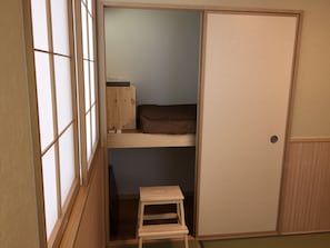 A traditional Japanese-style room with a sliding door, a small wooden bench, and a low bunk bed.