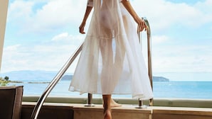 A woman in a white dress standing on a balcony with a view of the sea. - Domes Noruz Chania, Autograph Collection - Adults Only (Chania)