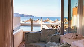Un balcone con vista sul mare, un'area salotto con cuscini e una porta vetrata che dà su una zona piscina.