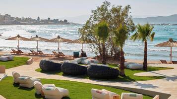 Un área de descanso en la playa con sillones, sombrillas y una zona verde con pufs.