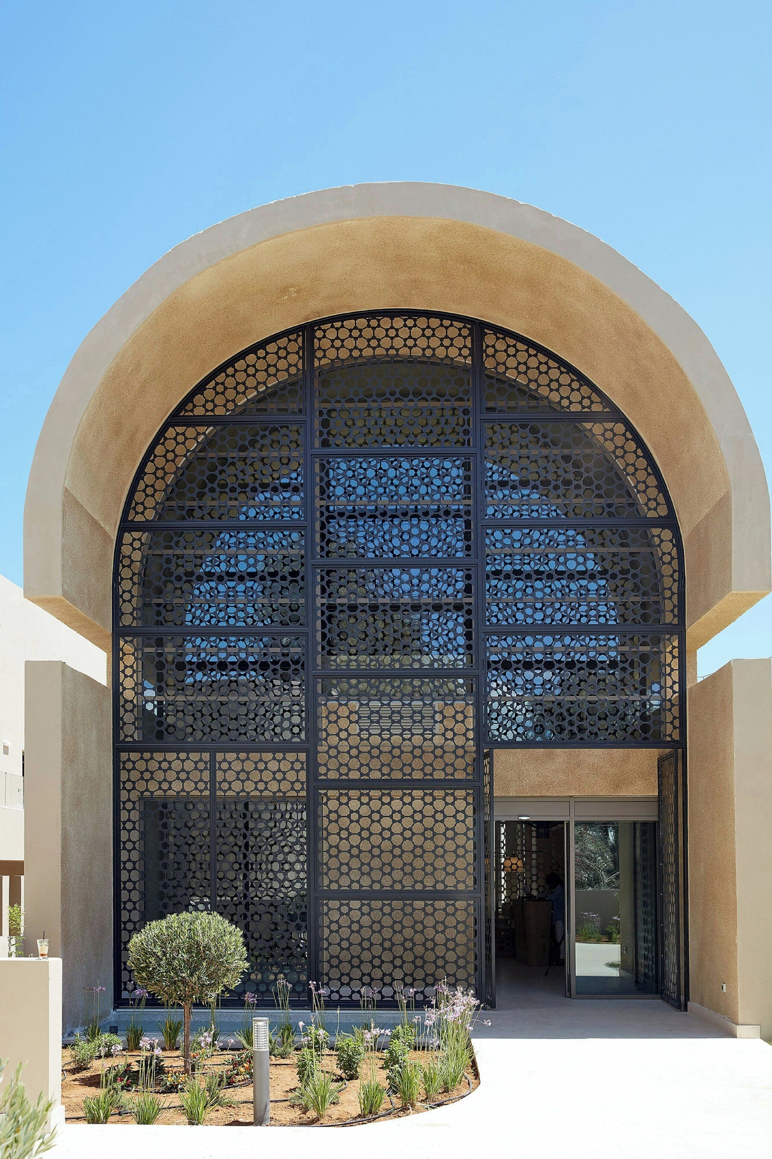 A modern building with a large arched entrance, a geometric facade, and a landscaped garden area.