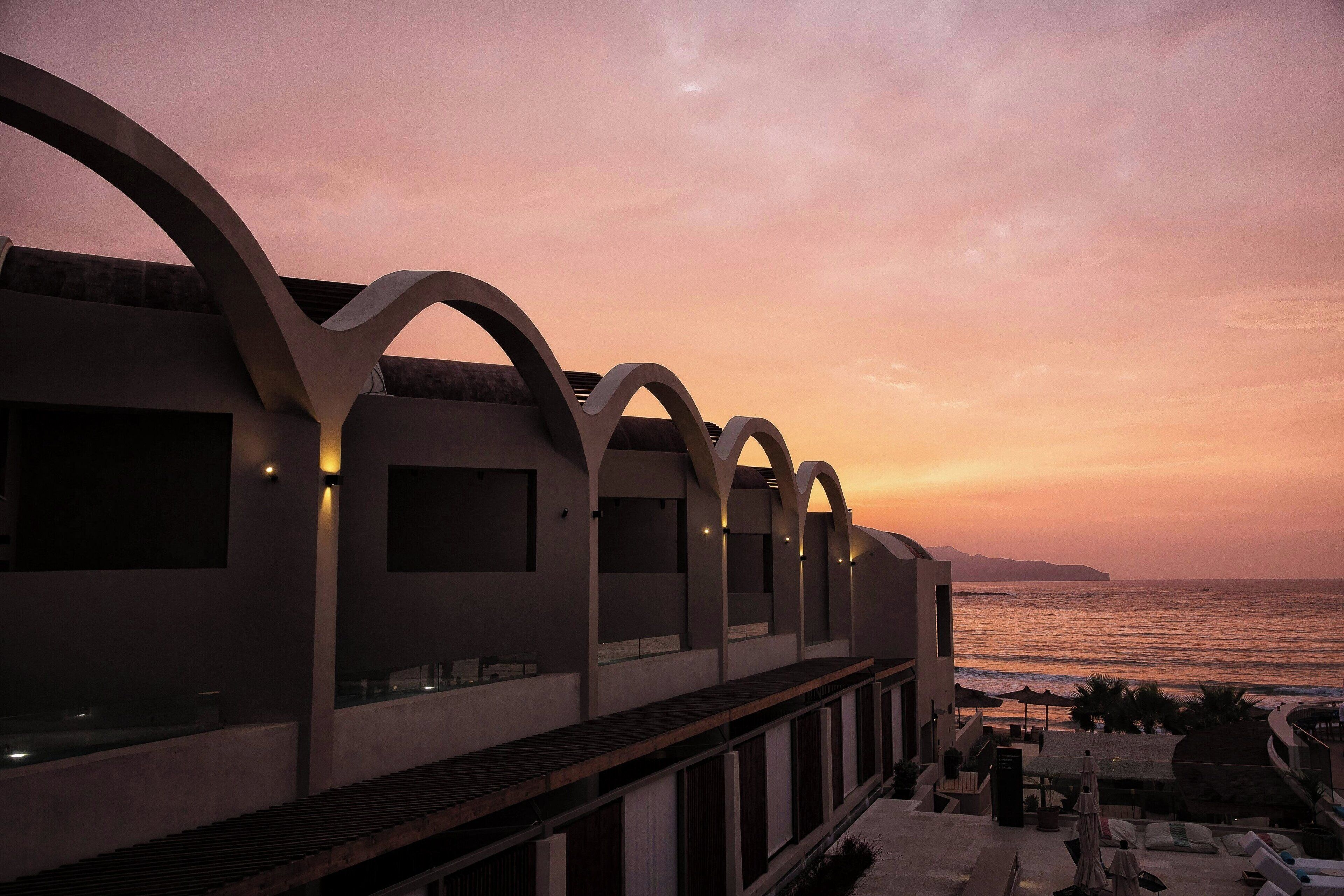 A modern building with arched balconies overlooking the sea at sunset.