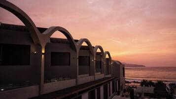 A modern building with arched balconies overlooking the sea at sunset.