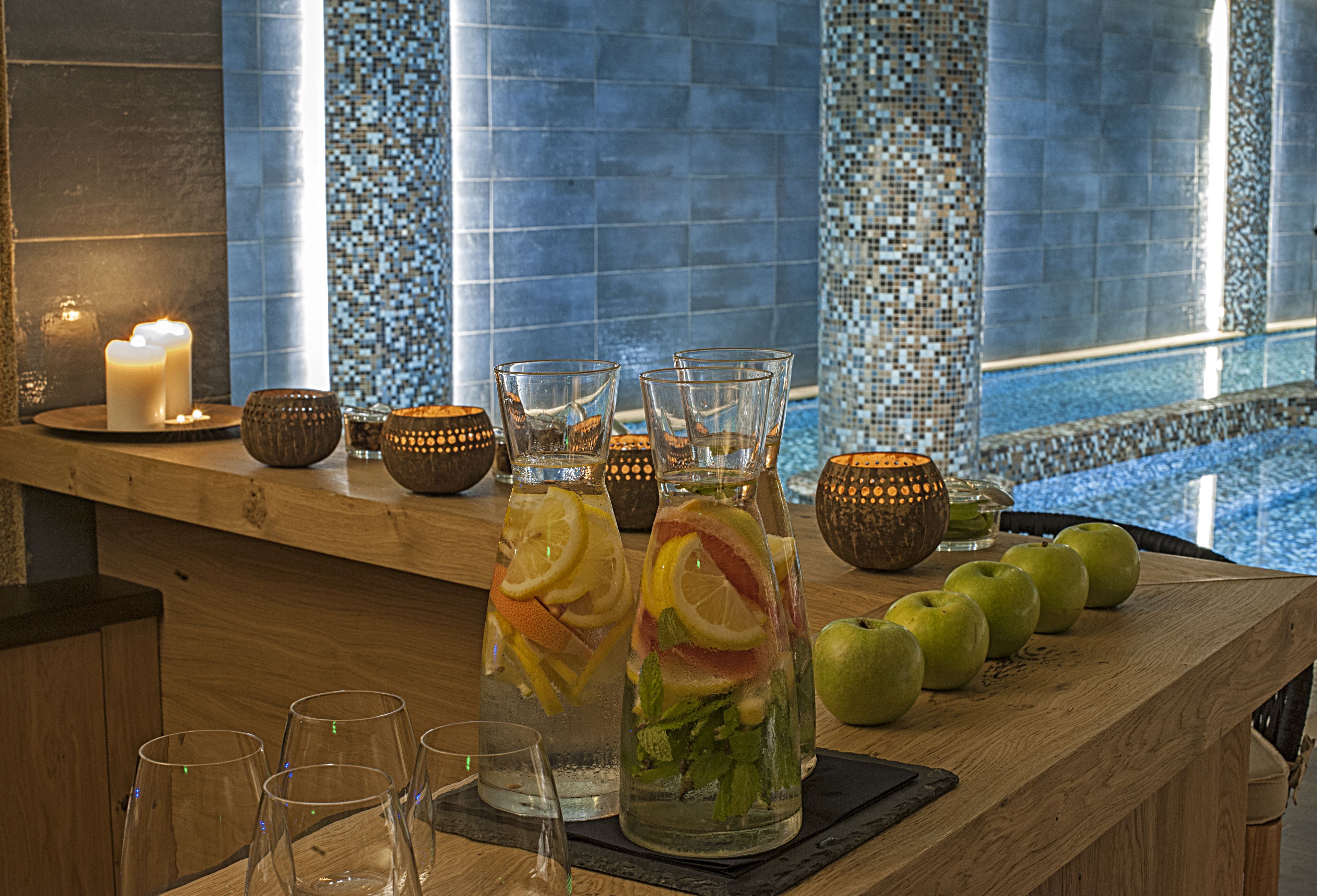 A bar area with a wooden counter, glasses, bottles, and apples.