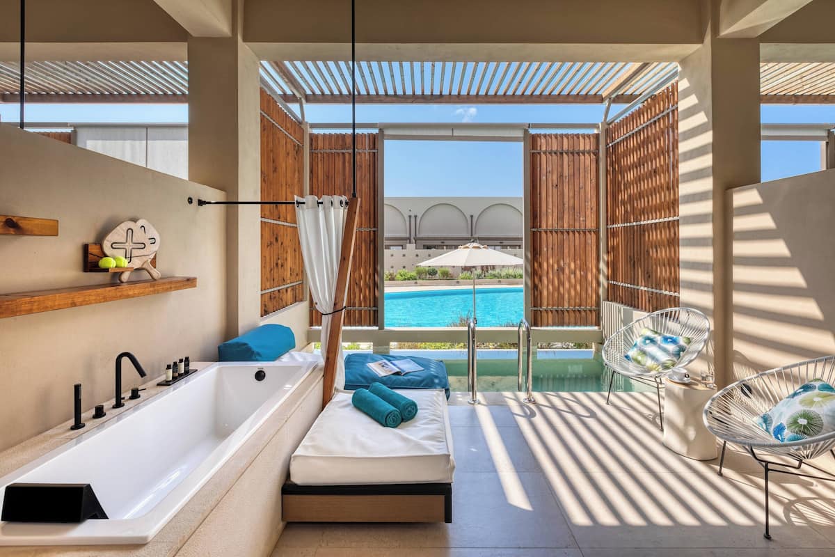 Ein modernes Badezimmer mit einer Badewanne, einem kleinen Nachttisch und einem Fenster mit Blick auf einen Pool.