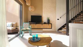 A modern living room with a sofa, a wooden coffee table, a television, and a staircase.