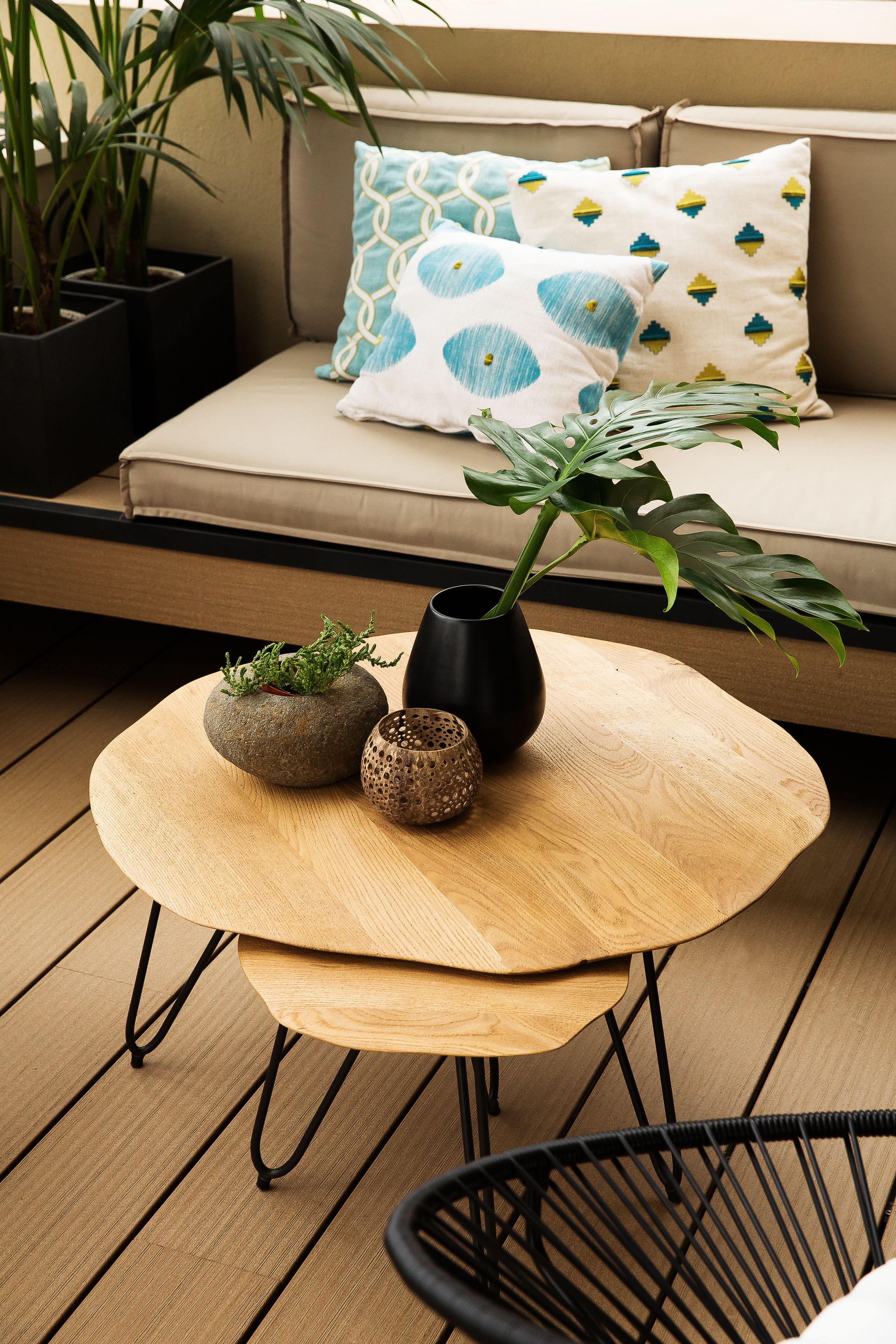 A wooden table with two vases and a plant, a black chair, and a beige sofa with patterned cushions.